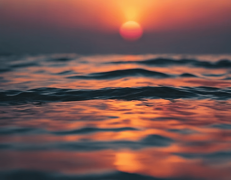 Sunset over ocean waves with orange and pink reflections on the water.
