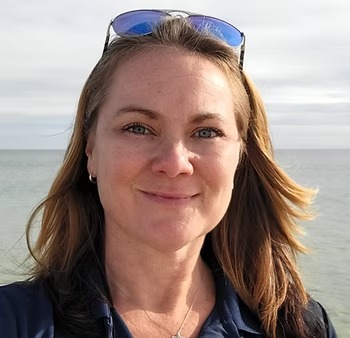 Smiling woman with sunglasses on head, standing by the sea.