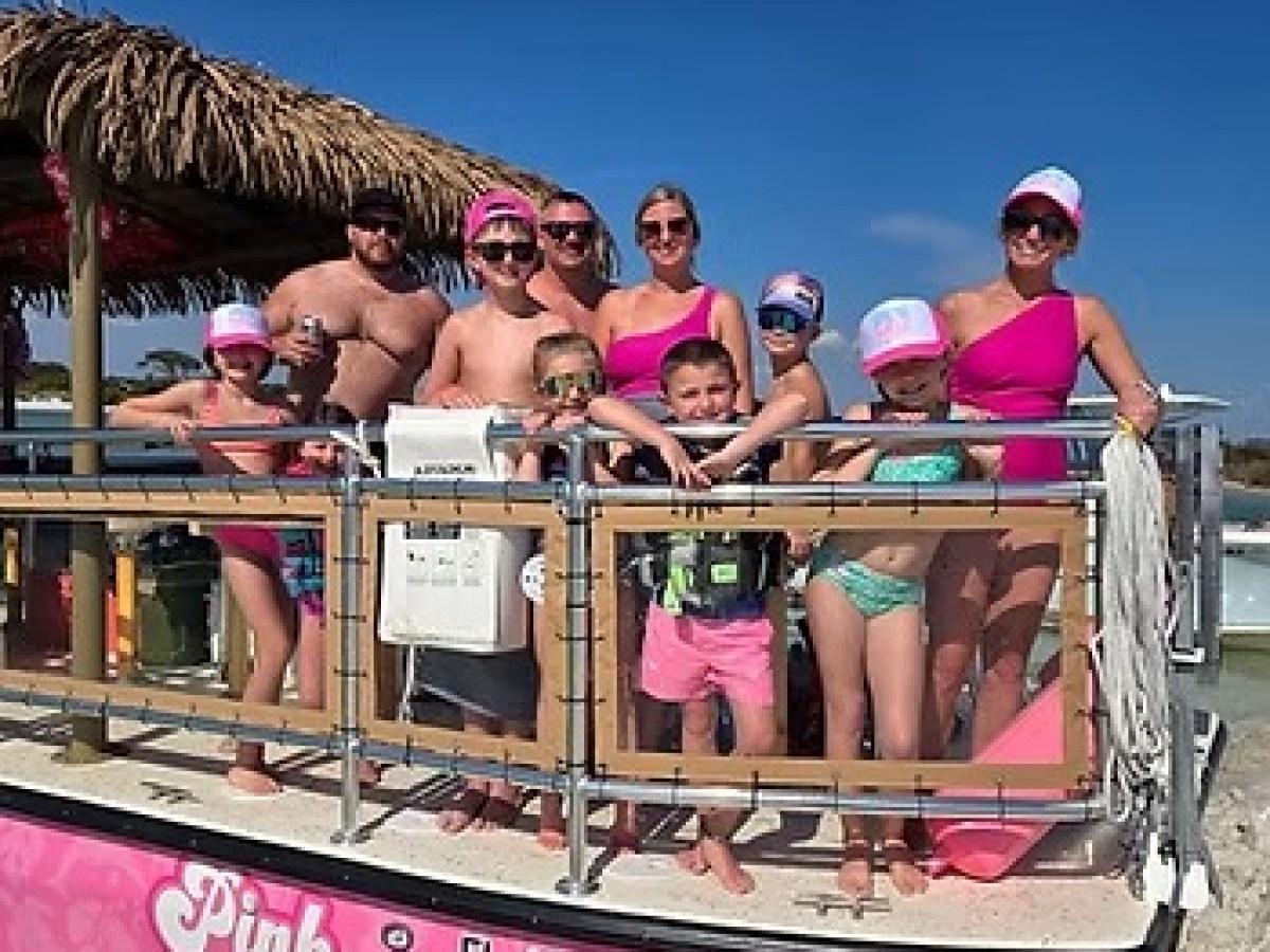 Group of people on a pink boat named 'Pink Pearl' on a sunny day.