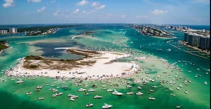 Aerial view of a crowded beach and numerous boats in turquoise water near a coastal city.