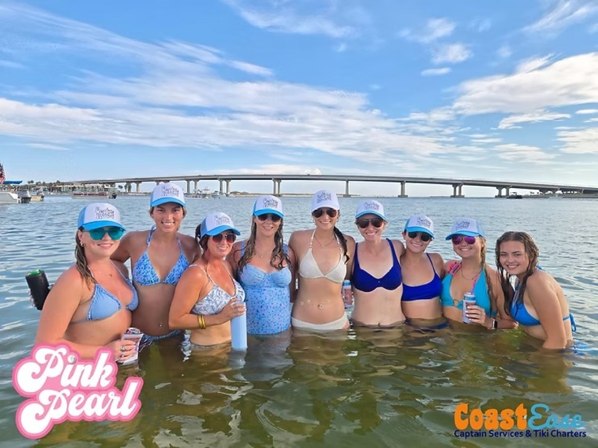 Group of women in swimsuits and caps standing in water, with a bridge in the background.