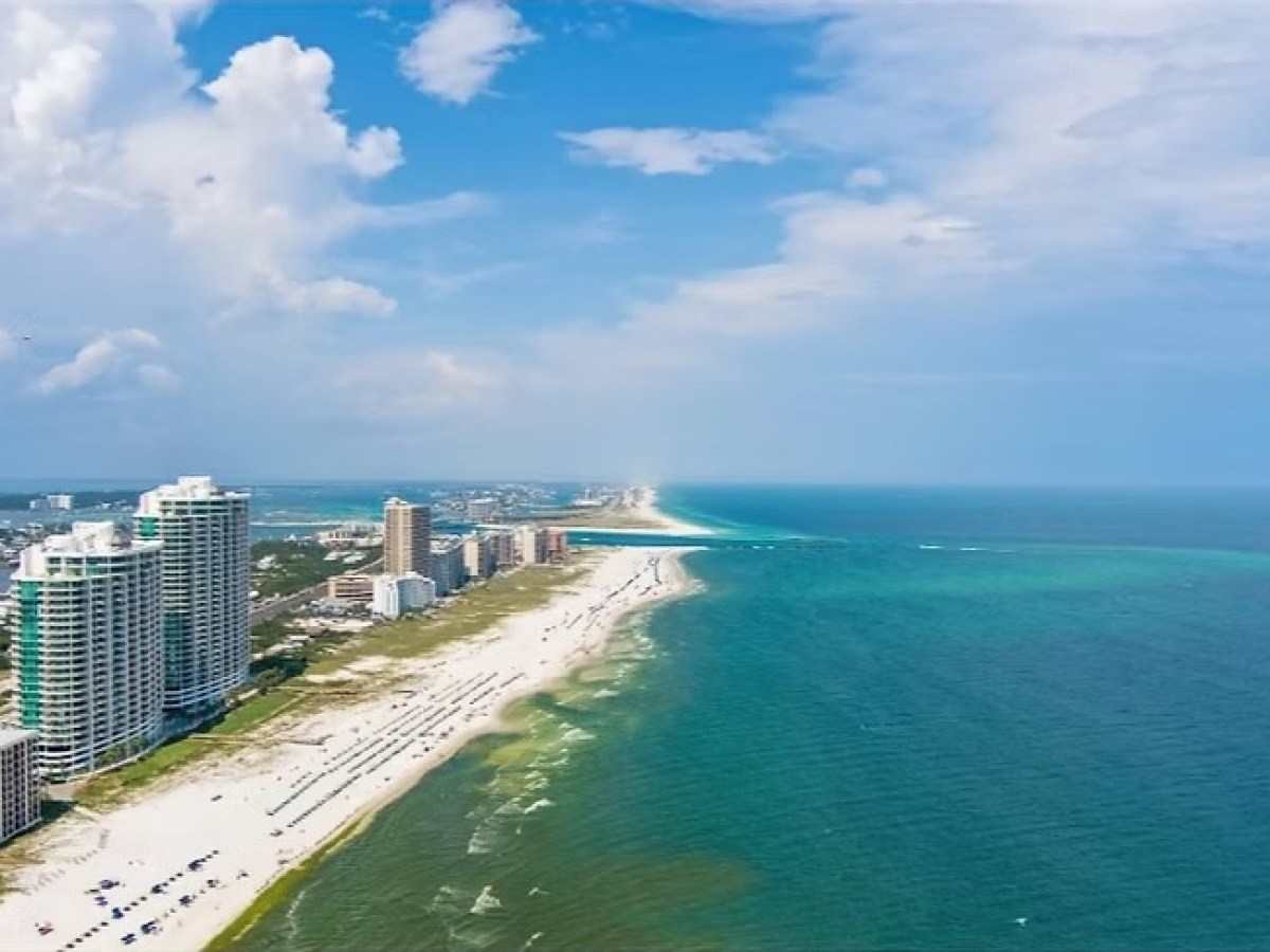 Aerial view of beach with tall buildings, green ocean, and blue sky.