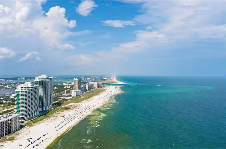 Aerial view of beach with tall buildings, green ocean, and blue sky.