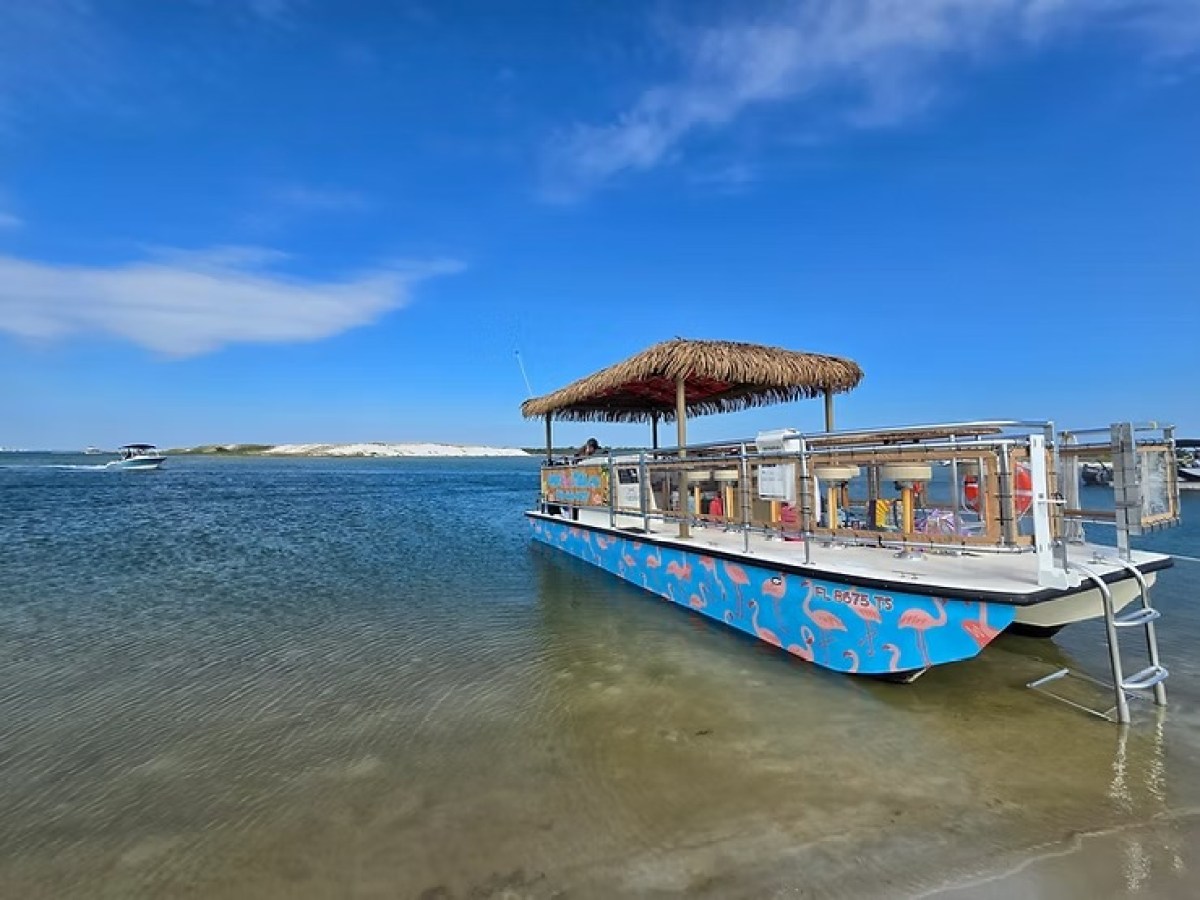 Colorful boat with a thatched roof docked at a beach under a clear blue sky.