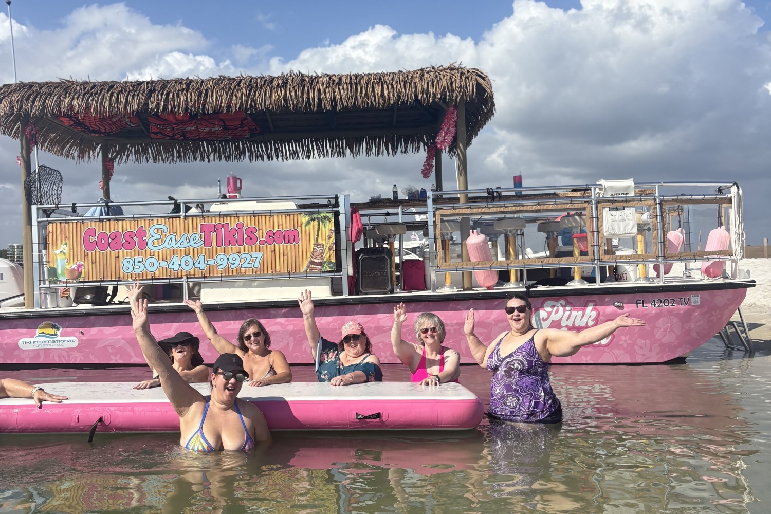 Group of people in water waving near a pink boat on a sunny day.