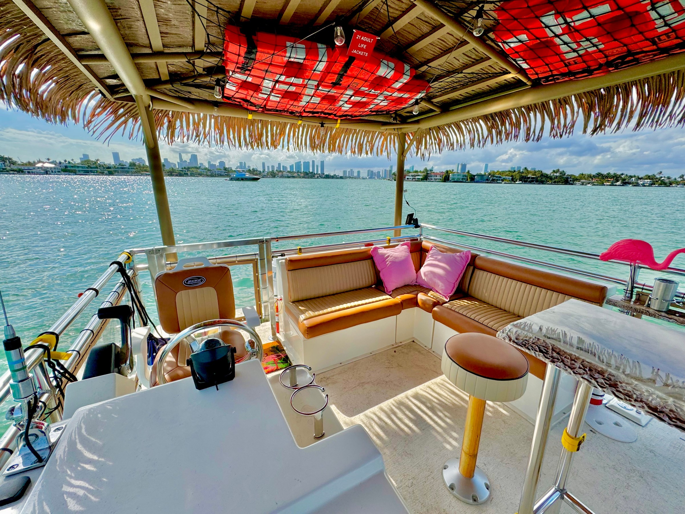 Boat deck with seating, bar stools, and city skyline view.