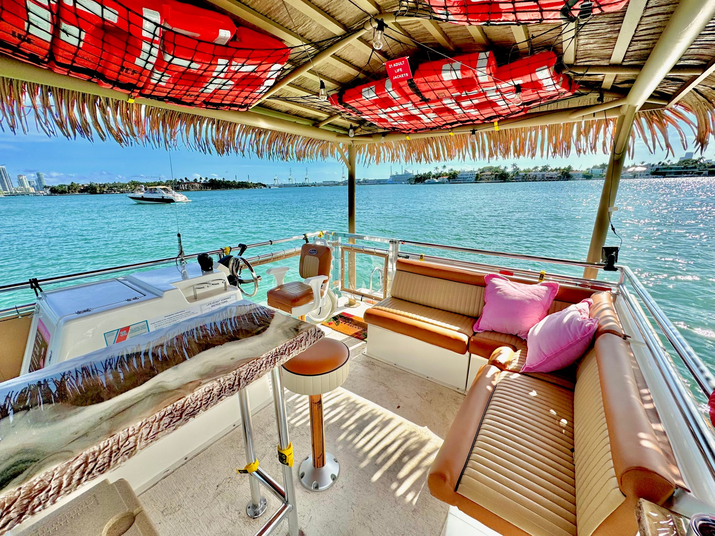 A tiki-style boat deck with seating, tropical roof, and view of water and another boat in the distance.