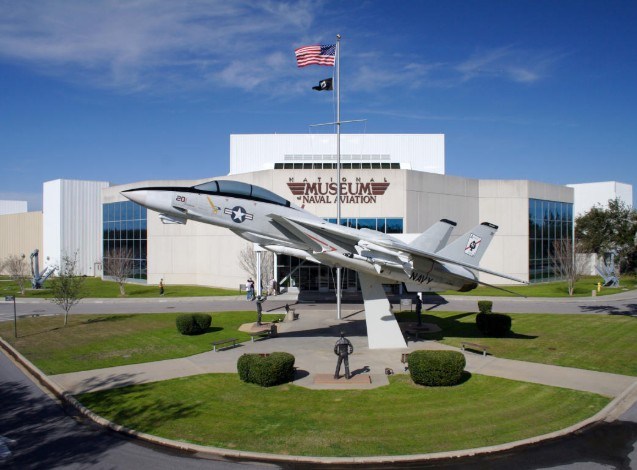 Navy jet on display outside the Museum of Naval Aviation with flags flying above.
